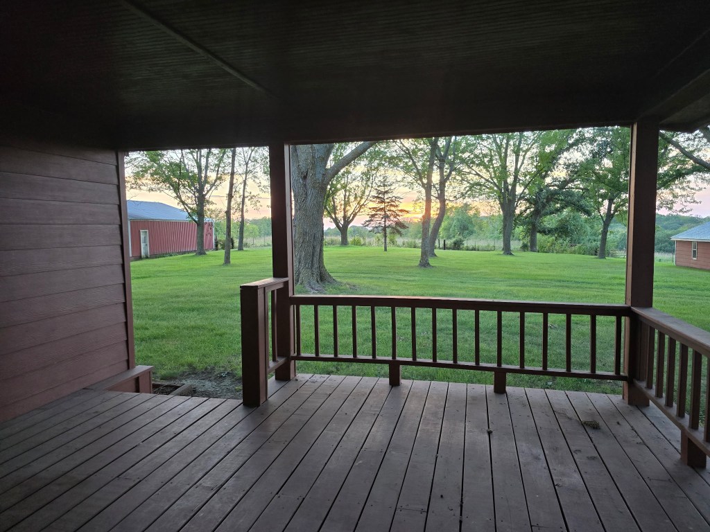 Sunset through the trees, viewed from the covered porch of the old farmhouse with the red barn at left